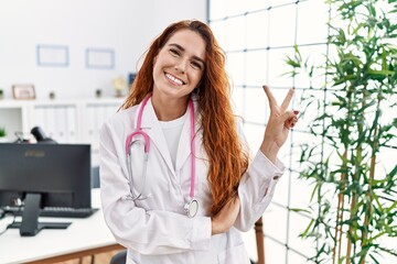 Young redhead woman wearing doctor uniform and stethoscope at the clinic smiling with happy face...