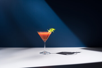 Bloody Mary decorado con hoja de apio en copa de cóctel sobre fondo azul	
