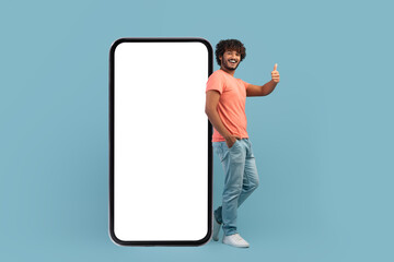 Happy indian man posing by big smartphone, showing thumb up