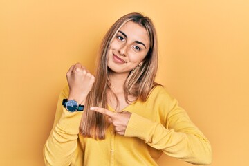 Beautiful hispanic woman wearing casual yellow sweater in hurry pointing to watch time, impatience, looking at the camera with relaxed expression