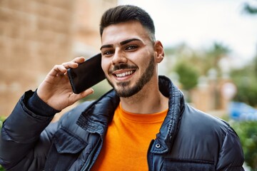 Handsome hispanic man with beard smiling happy and confident at the city wearing winter coat...