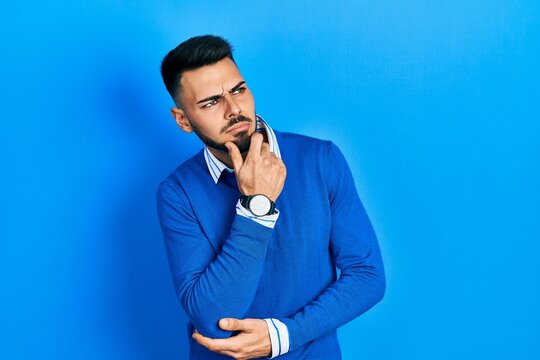 Young hispanic man with beard wearing casual blue sweater thinking worried about a question, concerned and nervous with hand on chin