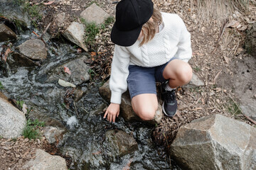 Young girl sitting by a creek touching the water - obrazy, fototapety, plakaty