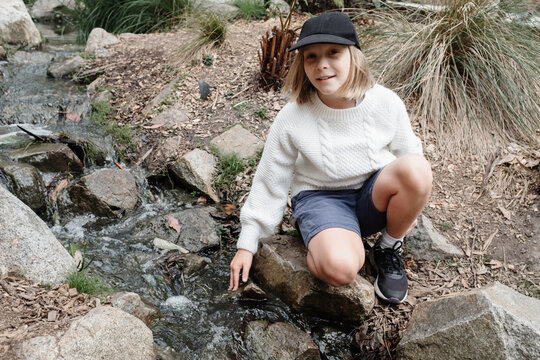 Young girl sitting by a creek touching the water