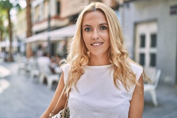 Young blonde woman smiling confident at street
