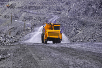 Heavy truck pours the road with water in the iron ore quarry. Dust removal, protection of the environment. Irrigation of the road from dust