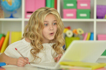 Cute girl ding home work with laptop at desk
