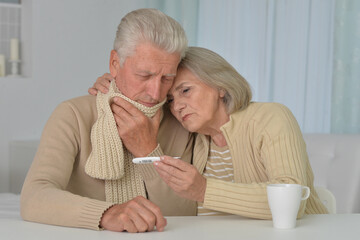 ill senior couple with thermometer at home