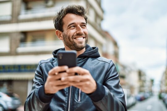 Handsome hispanic man with beard smiling happy outdoors using smartphone