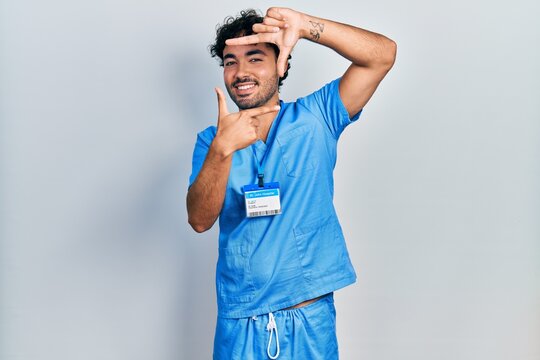 Young hispanic man wearing blue male nurse uniform smiling making frame with hands and fingers with happy face. creativity and photography concept.