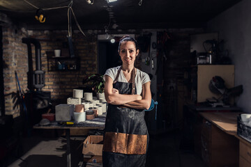 Portrait of craftswoman in apron working in her workshop making decorative concrete vase.