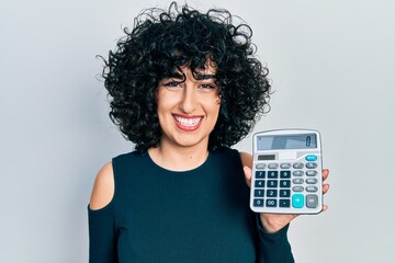 Young middle east woman showing calculator device looking positive and happy standing and smiling...