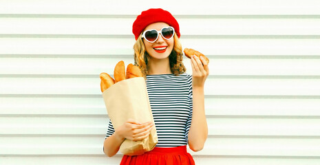 Portrait pretty woman eating croissant wearing red beret holding paper bag with long white bread baguette on white wall background