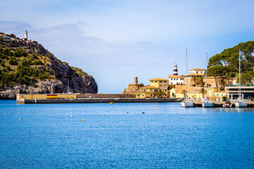Photography of the tranquil harbor basin of port de soller with three sailboats and one motorboat moored at the pier. Lighthouse Far de sa creu and beacon far del cap gros in the background. - obrazy, fototapety, plakaty