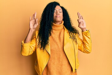 Middle age african american woman wearing wool winter sweater and leather jacket relaxed and smiling with eyes closed doing meditation gesture with fingers. yoga concept.