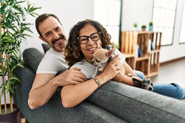 Middle age hispanic couple smiling happy sitting on the sofa with dogs at home.