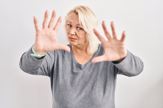Middle age caucasian woman standing over white background doing frame using hands palms and fingers, camera perspective