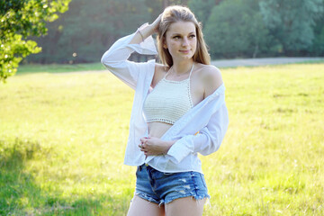 Pretty young woman wears hot pants, open blouse and top belly free and smiles friendly on sunny...