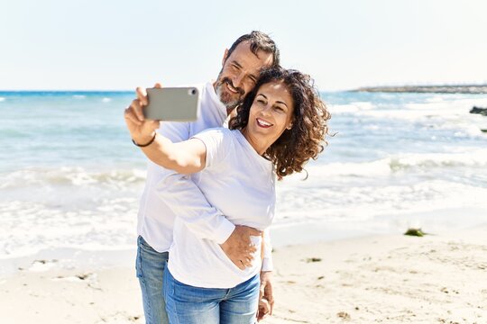 Middle age hispanic couple smiling happy and hugging making selfie by the smartphone at the beach.