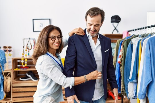 Middle age man and woman smiling confident choosing clothes at clothing store