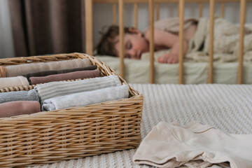 Baby clothes in a wicker container against the background of a sleeping baby. Vertical clothing...