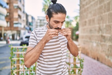 Young hispanic man rolling cigarette at street