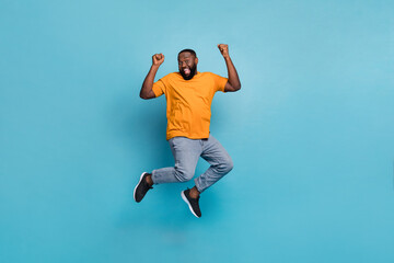 Fototapeta na wymiar Photo of attractive lucky guy dressed orange t-shirt jumping high rising fists isolated blue color background