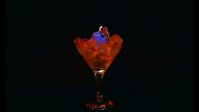 Orange flame in a cocktail glass with strong alcohol with ice. On a dark background, a glass with burning ice. Blue reflexes on ice in a glass of burning strong alcohol.