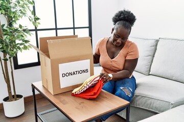 Young african american woman folding clothes to donate at home