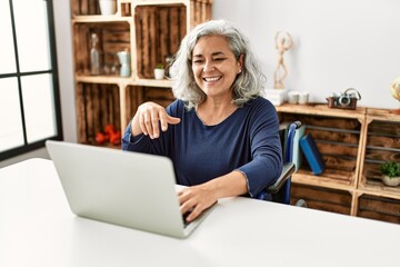 Middle age grey-haired disabled woman having video call sitting on wheelchair at home.