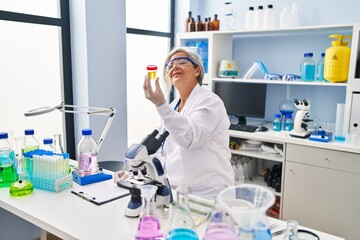 Fototapeta na wymiar Middle age woman wearing scientist uniform holding urine analysis test tube at laboratory