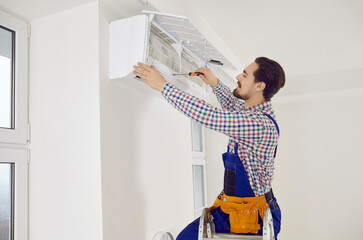 Technician repairing a modern AC system on his typical day at work. Young repairman in an overall...