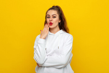 Oops. Embarrassed brunette girl 20s use hand cover mouth looks with a having mysterious facial expression, being guilty and hoping that nobody will know about her fault, stands over yellow background