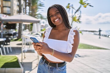 Young african american girl smiling happy using smartphone at the promenade