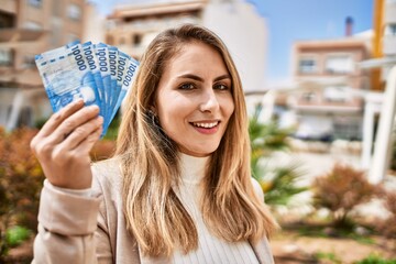 Young blonde woman smiling confident holding chilean pesos banknotes at street