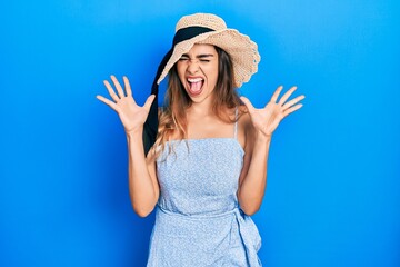 Young hispanic girl wearing summer hat celebrating mad and crazy for success with arms raised and...