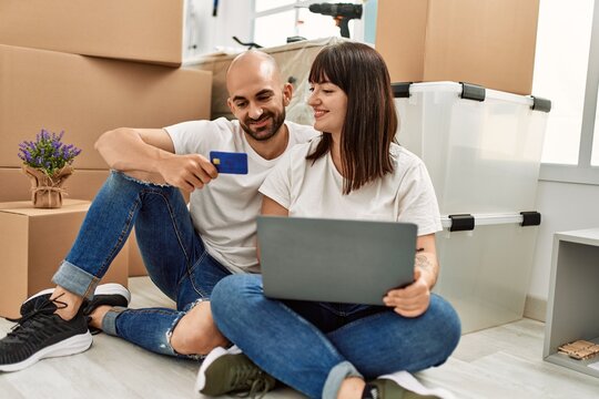 Young hispanic couple smiling happy using laptop and credit card at new home.