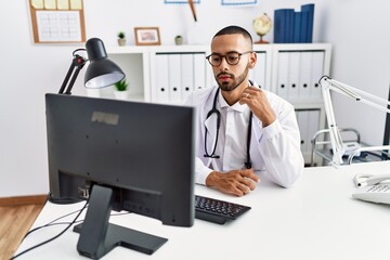 Young hispanic man wearing doctor uniform having video call at clinic