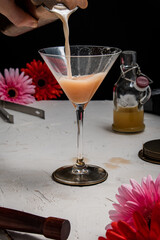 A freshly made French Martini cocktail being strained into a martini glass, on a white background and styled with bar equipment and red and pink flowers.