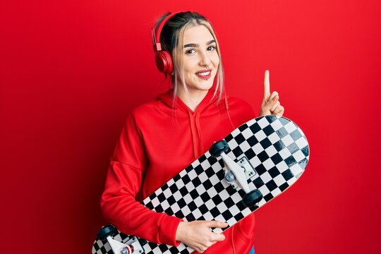 Young modern girl holding skate wearing headphones smiling with an idea or question pointing finger with happy face, number one