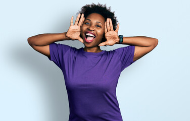 African american woman with afro hair wearing casual purple t shirt smiling cheerful playing peek a...