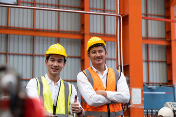 Selective focus at Asian men mechanical engineer, wearing safety equipment. While doing machine maintenance and safety control inside of factory area. With blurred background of heavy machine.