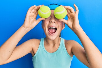 Beautiful brunette little girl holding tennis ball close to eyes angry and mad screaming frustrated...