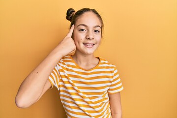 Beautiful brunette little girl wearing casual striped t shirt smiling pointing to head with one finger, great idea or thought, good memory