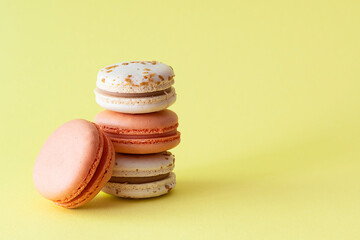 Beige and pink macaroons lie on a yellow table. Light yellow background, text space