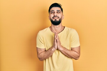 Fototapeta premium Handsome man with beard wearing casual yellow t shirt begging and praying with hands together with hope expression on face very emotional and worried. begging.