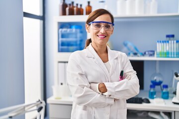 Middle age woman wearing scientist uniform standing with arms crossed gesture at laboratory