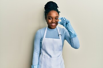 African american woman with braided hair wearing cleaner apron and gloves smiling and confident...
