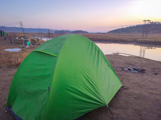 isolated camping tent at calm lake shore with dramatic sunrise colorful sky reflection at morning