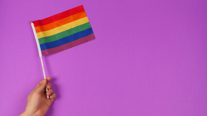 Hand hold a rainbow flag on purple background. LGBT CONCEPT..